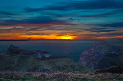 a sunset over the ocean with the sun setting on a mountain at Camelot Castle Hotel in Tintagel