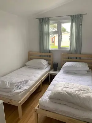 two twin beds in a room with a window at Chalets & Lodges at Atlantic Bays Holiday Park in Padstow