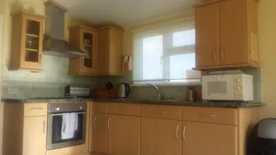 a kitchen with wooden cabinets and a sink and a microwave at Chalets & Lodges at Atlantic Bays Holiday Park in Padstow