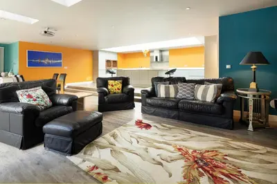 a living room with black leather furniture and a kitchen at Talland Bay Hotel, Looe in Talland