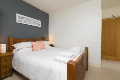 a bedroom with a white bed with a wooden headboard at Oystercatcher in St Ives