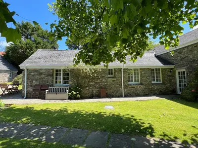 a stone house with a bench in the yard at Almond Tree Cottage in Lanteglos