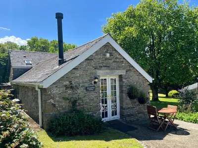 a small stone cottage with a table and a chair at Almond Tree Cottage in Lanteglos