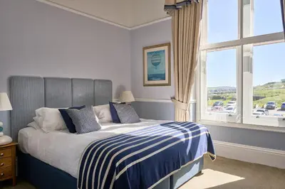 a bedroom with a bed with blue and white sheets and a window at The Headland Hotel and Spa in Newquay