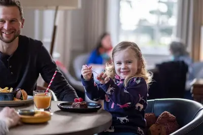 a little girl sitting at a table eating food at Fowey Hall Hotel in Fowey