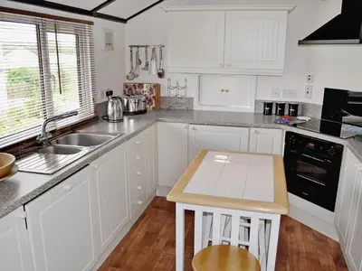 a white kitchen with white cabinets and a sink at Driftwood in St Merryn