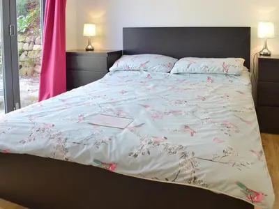 a bed with a white bedspread with pink flowers on it at Kataluma in Germoe