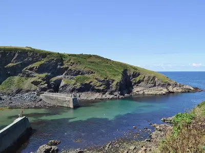 a large body of water next to a cliff at Silvershell View in Port Isaac