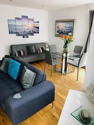 a living room with a blue couch and a glass table at Seaview, Luxury apartment, 2 min walk to Porth Beach in Newquay