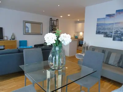 a vase with white flowers on a glass table in a living room at Seaview, Luxury apartment, 2 min walk to Porth Beach in Newquay