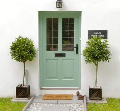 a green door on a white house with two potted plants at Caroe Farm House in Otterham