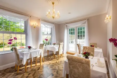 a dining room with tables and chairs and windows at Rockleigh Place in St Austell