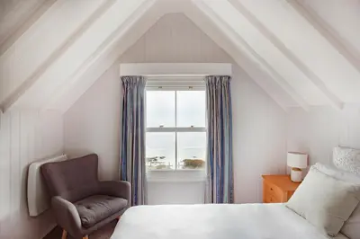 a bedroom with a bed and a chair and a window at The Bay Hotel in Coverack