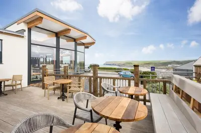 a deck with tables and chairs and a view of the water at Oystercatcher Apartments in Polzeath