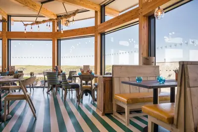 a restaurant with tables and chairs and large windows at Oystercatcher Apartments in Polzeath