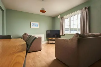 a living room with two couches and a table and a television at Oystercatcher Apartments in Polzeath