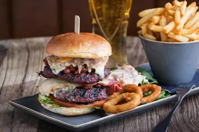 a hamburger on a plate with onion rings and a cup of fries at Oystercatcher Apartments in Polzeath