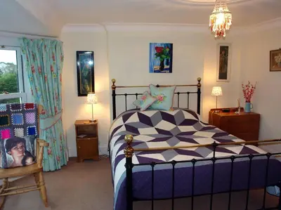 a bedroom with a bed and a chair and a chandelier at Heightley House in Tintagel