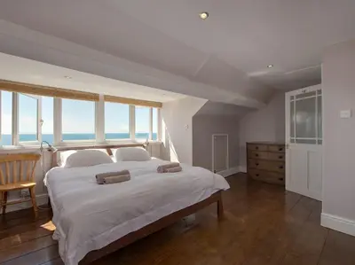 a bedroom with a large white bed with windows at The Captains House in Downderry