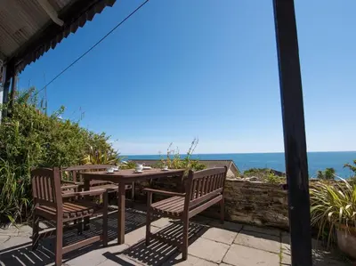a table and chairs on a patio with the ocean in the background at The Captains House in Downderry