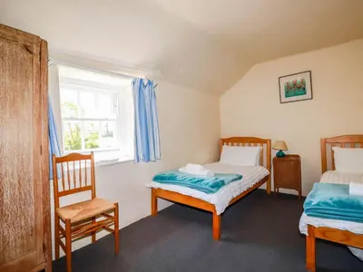 a bedroom with two beds and a chair and a window at Polcreek Farmhouse in Veryan