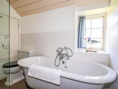 a bathroom with a tub and a bird in a window at Polcreek Farmhouse in Veryan