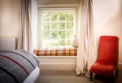 a bedroom with a window and a red chair at Trewornan Manor in Wadebridge