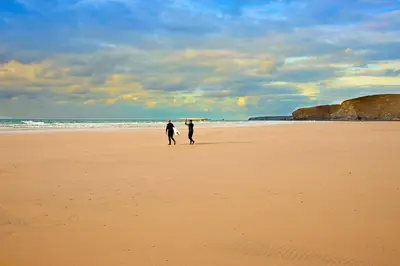 two people walking on a beach with a surfboard at Waves Apartments in Newquay