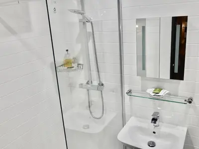 a white bathroom with a shower and a sink at Talehay Cottages in Looe