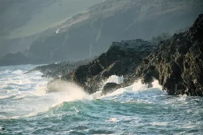 a wave in the ocean near a rocky coastline at Talehay Cottages in Looe