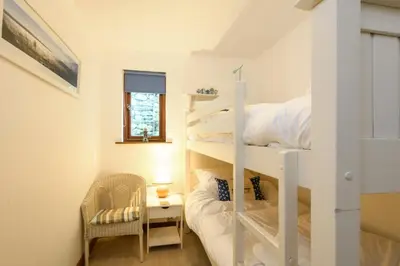 a small room with a bunk bed and a chair at White Lodge Apartments in Mawgan Porth