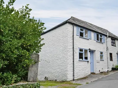 a white building with a blue door and a tree at Ostlers in Boscastle