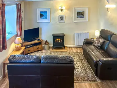 a living room with a leather couch and a fireplace at Ostlers in Boscastle