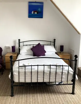 a bedroom with a bed with white sheets and purple pillows at Donnington Guesthouse in Truro