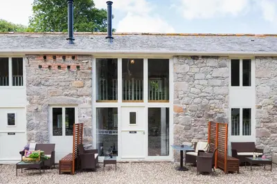 an exterior view of a stone building with patio furniture at Red River Stables - Peaceful, beautiful grounds, swimming pool, central location for West Cornwall in Camborne