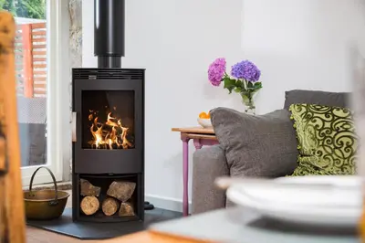 a wood stove in a living room with a couch at Red River Stables - Peaceful, beautiful grounds, swimming pool, central location for West Cornwall in Camborne