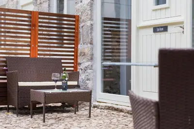 a patio with two chairs and a table with wine glasses at Red River Stables - Peaceful, beautiful grounds, swimming pool, central location for West Cornwall in Camborne