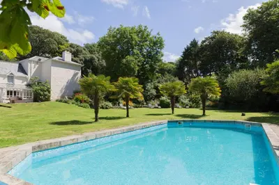a large swimming pool in a yard with trees at Red River Stables - Peaceful, beautiful grounds, swimming pool, central location for West Cornwall in Camborne