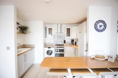 a kitchen with white cabinets and a wooden table at Stunning Two Bed Sea View Apartment with Pool & Gym in Newquay