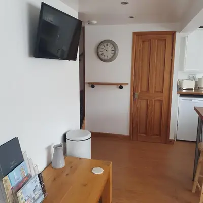 a living room with a table and a clock on the wall at Chynoweth Mews in Newquay