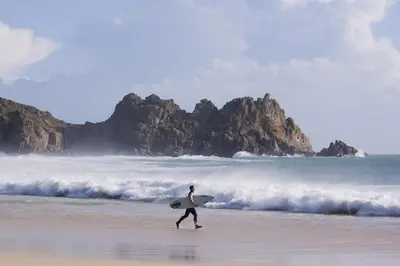 a man walking on the beach with a surfboard at Cargurra Farm in Boscastle