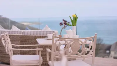 a table with two chairs and a table with a vase with flowers at Boskerris Hotel in St Ives