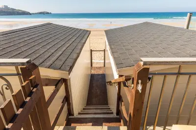 a house on the beach with the ocean in the background at Tolcarne Beach Cabins in Newquay