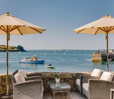 a patio with chairs and tables with a view of the water at The Idle Rocks in Saint Mawes