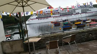 a cruise ship docked at a dock with chairs and an umbrella at Reed's of Fowey in Fowey