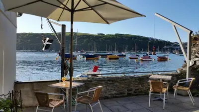 a table and chairs with an umbrella and boats in the water at Reed's of Fowey in Fowey