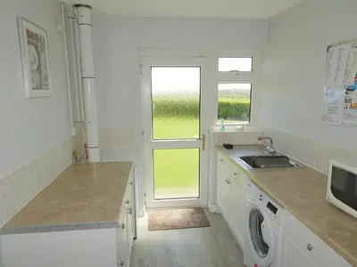 a white kitchen with a sink and a window at Tregoona in Crantock