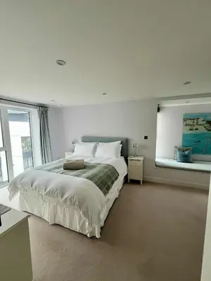 a white bedroom with a large bed and a window at 6 Ocean Gate apartment in Newquay