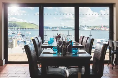 a dining room with a table with chairs and a view of the water at Chainlocker in Falmouth