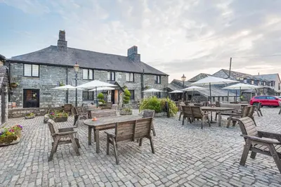 a patio with wooden tables and chairs and umbrellas at The Jamaica Inn, Bodmin, Cornwall - The Coaching Inn Group in Bolventor
